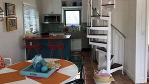 Una cocina compacta con armarios blancos, una mesa de comedor con sillas y una escalera que lleva a un nivel superior.