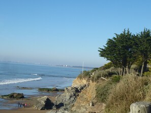 A coastal landscape with rocky cliffs, a beach, and a clear view of the ocean.