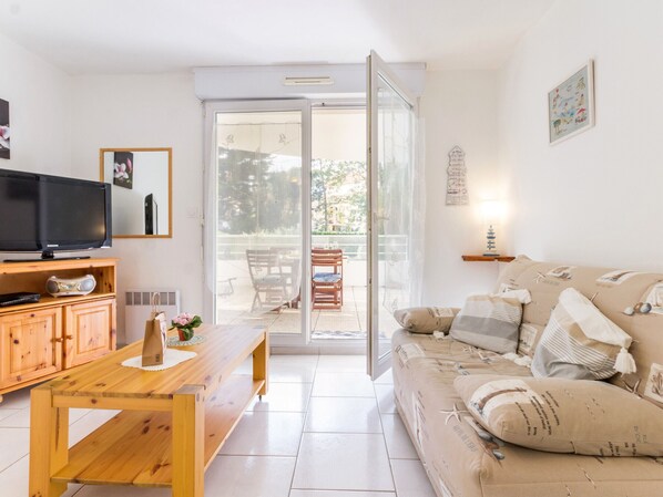 A living room with a television, wooden furniture, a sofa with patterned cushions, and a sliding glass door leading to an outdoor area.