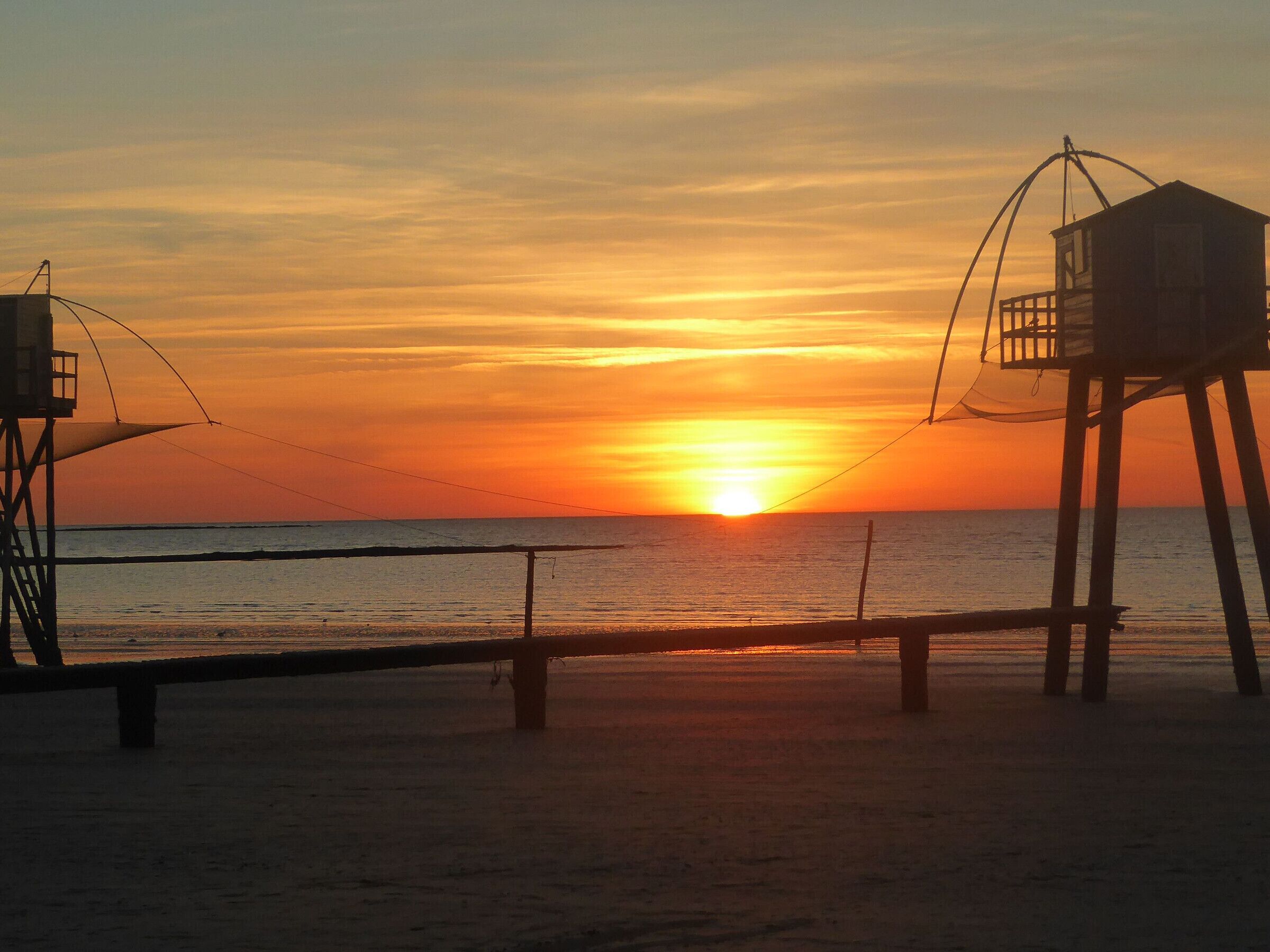 Una playa con una torre de salvavidas y una estructura sumergida, probablemente un muelle, durante el atardecer.