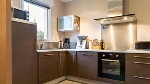 A modern kitchen with dark brown cabinets, a stainless steel range hood, a microwave, and an oven. - Cozy Wood Cottage with Spa, Garden, and Bikes - Near Nantes (Casson)