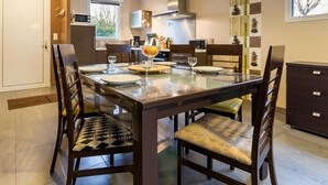 A dining area with a rectangular table set for four, surrounded by wooden chairs with patterned cushions. - Cozy Wood Cottage with Spa, Garden, and Bikes - Near Nantes (Casson)