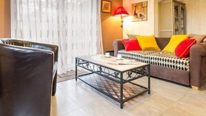 A living room with a sofa, a coffee table, a chair, and a lamp. - Cozy Wood Cottage with Spa, Garden, and Bikes - Near Nantes (Casson)