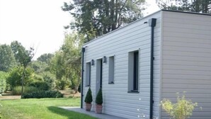 A modern single-story building with a flat roof, a small front porch, and a gravel driveway. - Cozy Wood Cottage with Spa, Garden, and Bikes - Near Nantes (Casson)