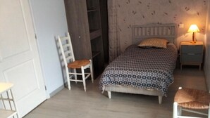 A bedroom with a bed, a chair, a nightstand, and a lamp.
