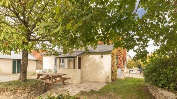 A small house with a patio, a wooden table, and a garden area.