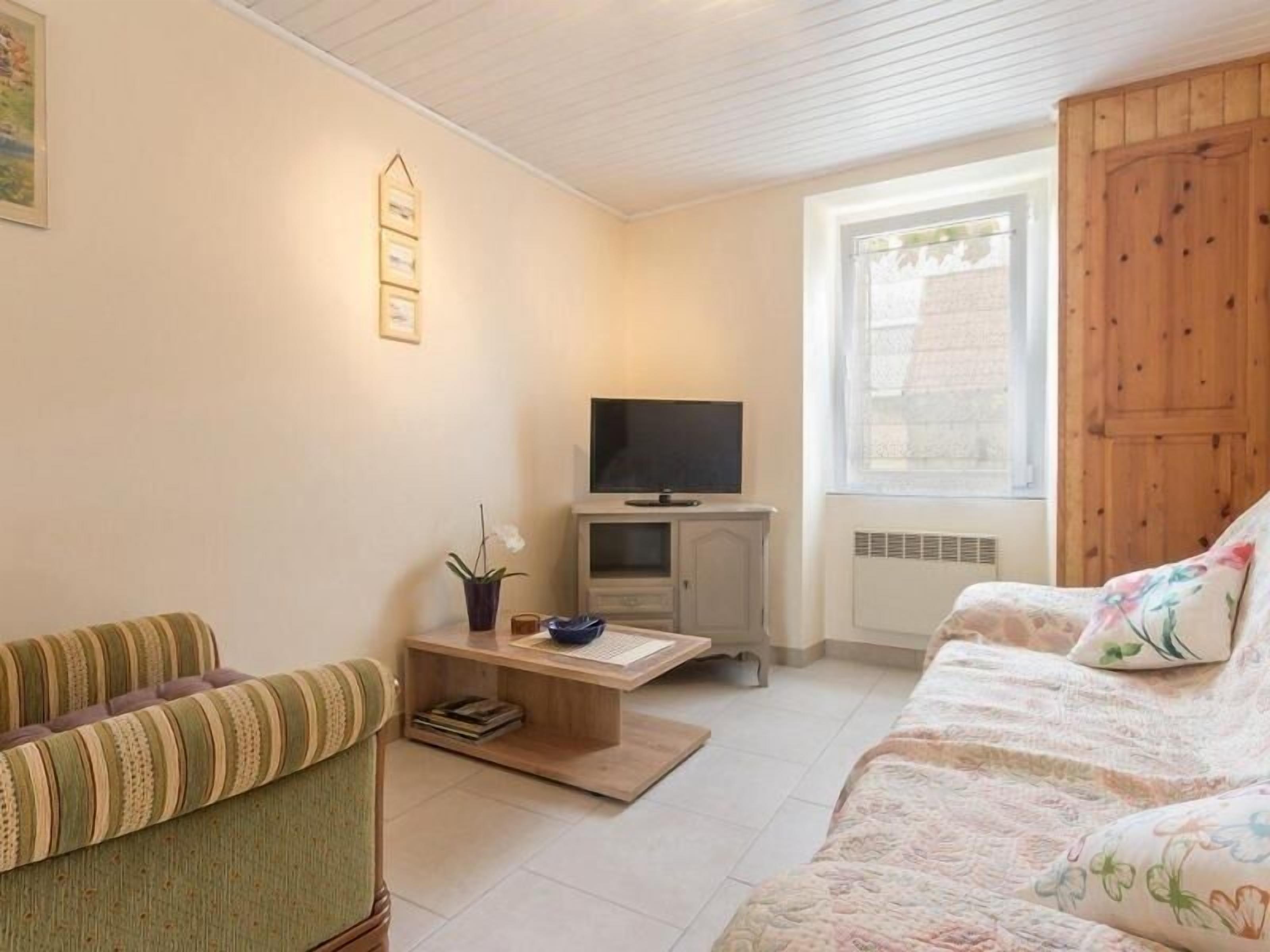 Una sala de estar acogedora con un sofá a rayas, un sofá estampado con flores, un televisor sobre un mueble de madera y una ventana con persianas.