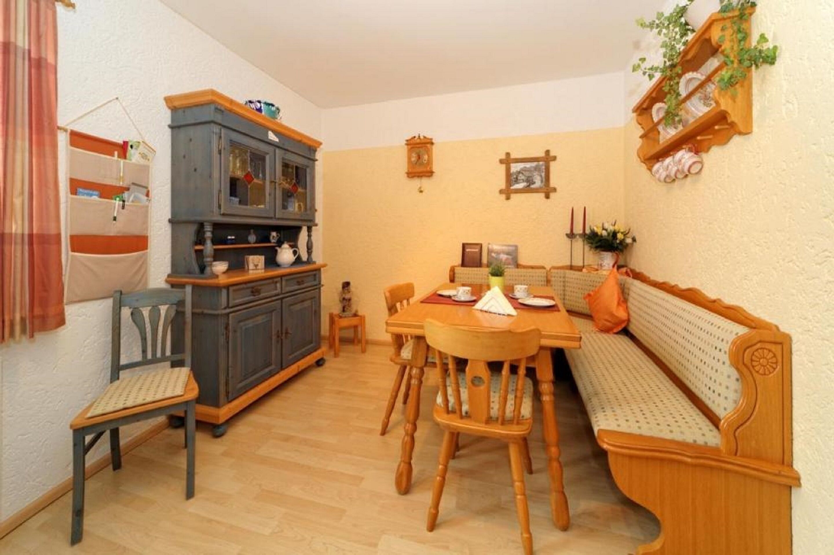 A dining area with a wooden table, chairs, a bench, a cabinet, and a shelf with decorative items.