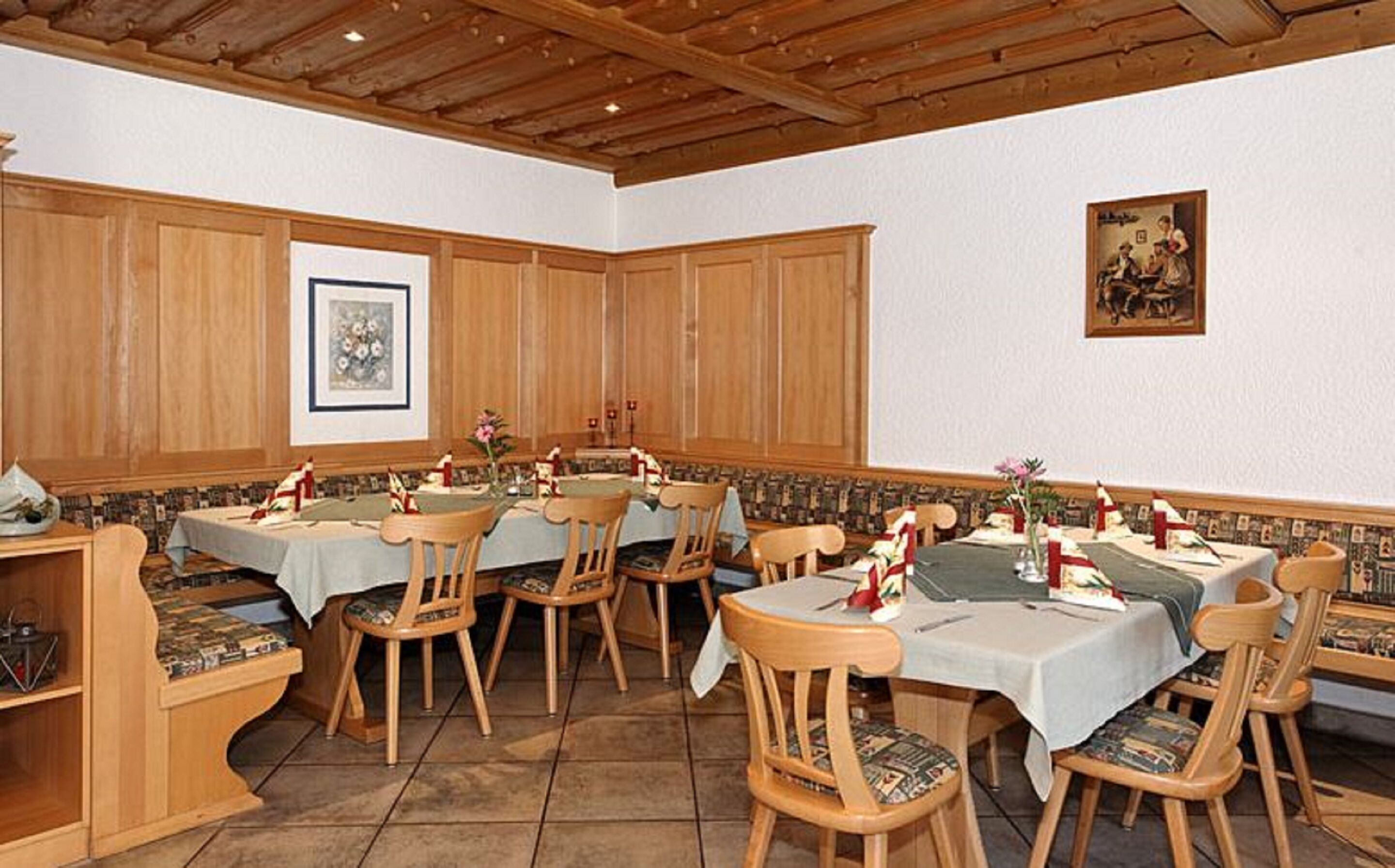 A dining area with wooden paneling, multiple tables with chairs, and a framed picture on the wall.