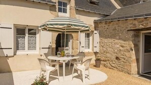A stone building with a patio area featuring a round table and chairs, an umbrella, and potted plants.