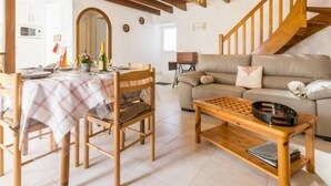 A cozy living room with a wooden staircase, a dining area with a table set for two, and a sofa with cushions.