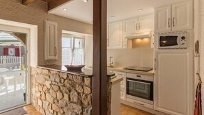 A kitchen with white cabinets, a stone accent wall, a built-in oven, and a microwave.