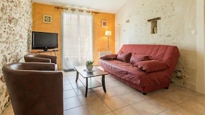 A living room with a red sofa, two armchairs, a coffee table, a TV, and a stone wall.