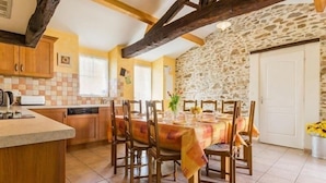 A rustic kitchen with wooden cabinets, a stone wall, and a dining area with a table set for four.