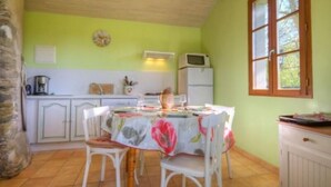 A kitchen with white cabinets, a dining table with floral tablecloth, and a window with wooden frames. - Renovated mill with enclosed garden near Pornic (Pornic-Le Clion sur Mer)