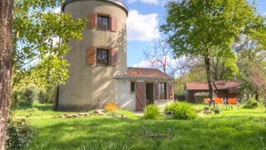 A round, two-story house with a conical roof, surrounded by a well-maintained garden and a smaller building with a red roof. - Renovated mill with enclosed garden near Pornic (Pornic-Le Clion sur Mer)