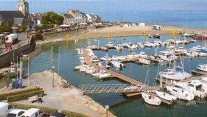 Un port de plaisance où sont amarrés de nombreux bateaux, une plage de sable et des bâtiments en arrière-plan.