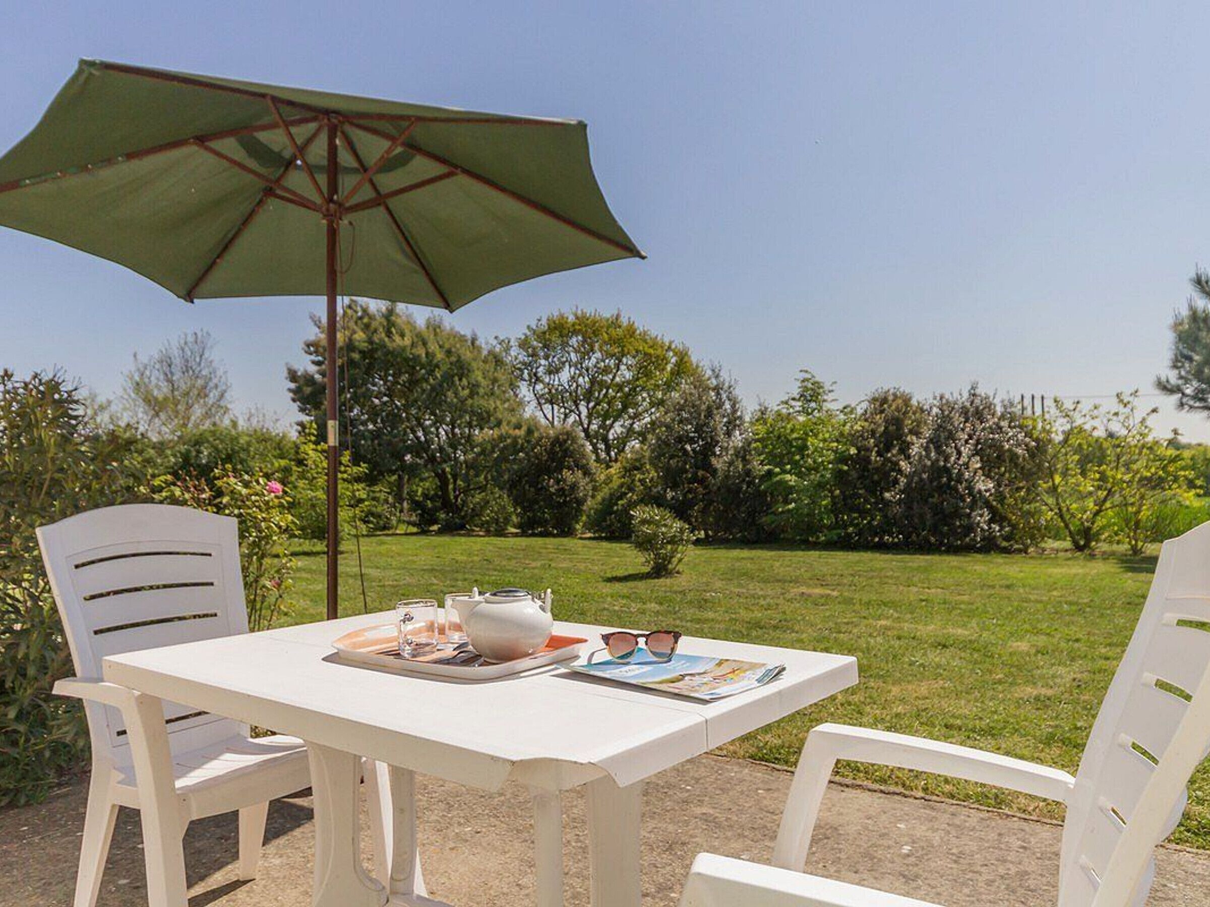 Une table blanche avec un parasol vert, deux chaises blanches et un magazine posé sur la table.