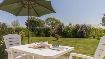 Une table blanche avec un parasol vert, deux chaises blanches et un magazine posé sur la table.