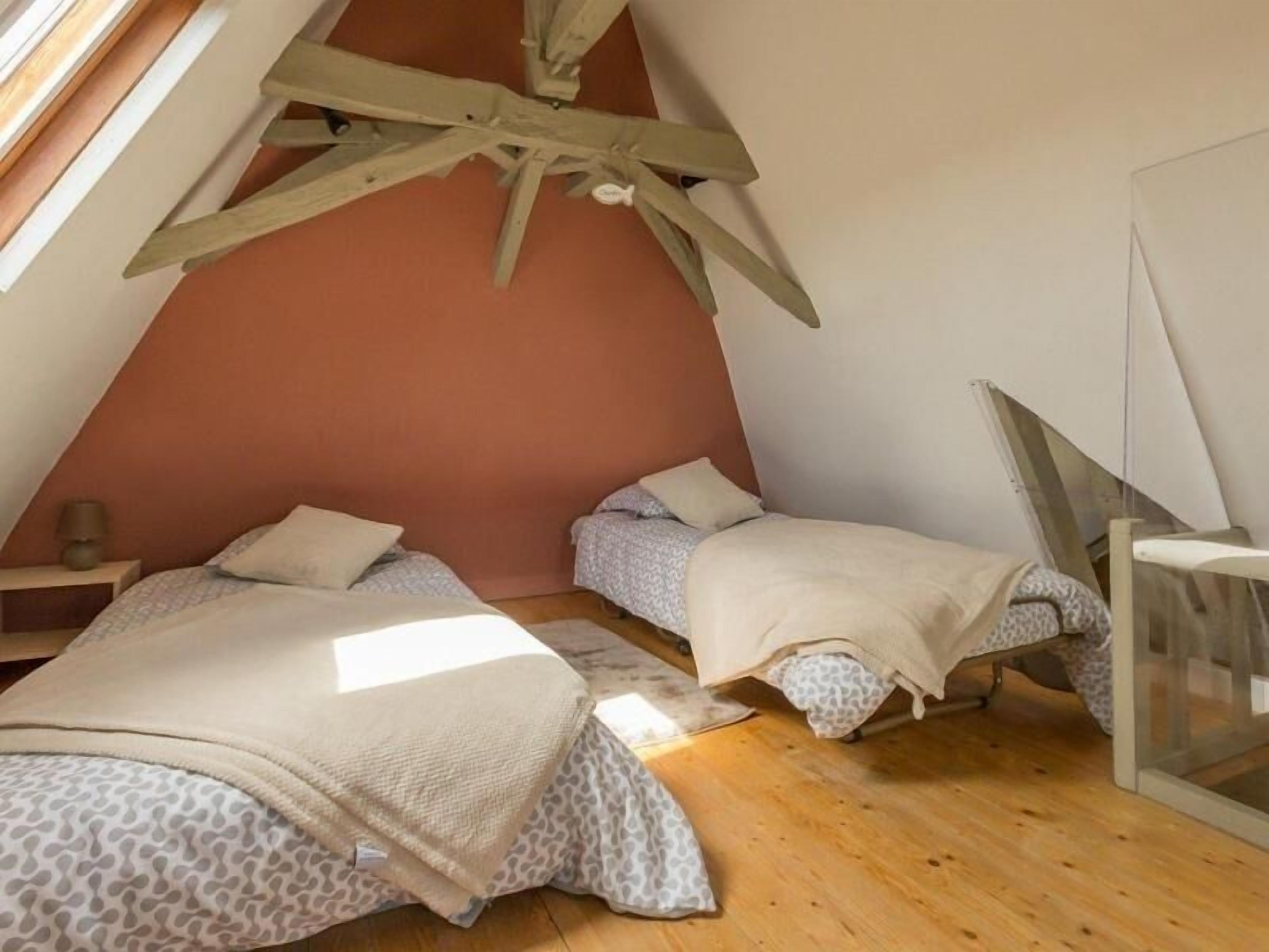 Ein kleines, dreieckiges Schlafzimmer im Dachgeschoss mit zwei Betten, Holzbalken und einem Fenster.
