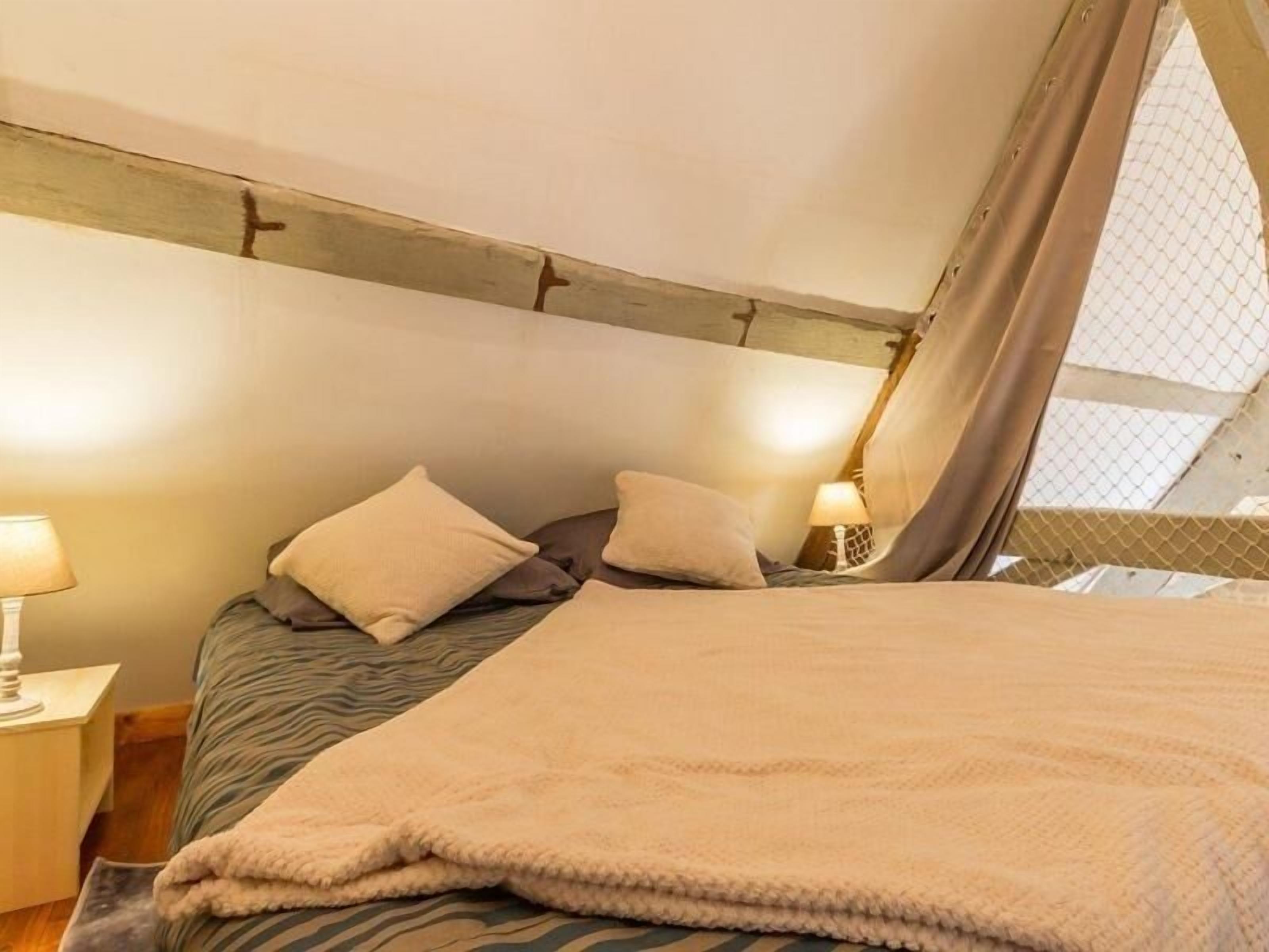 A cozy bedroom with a bed, pillows, a nightstand, and a lamp.