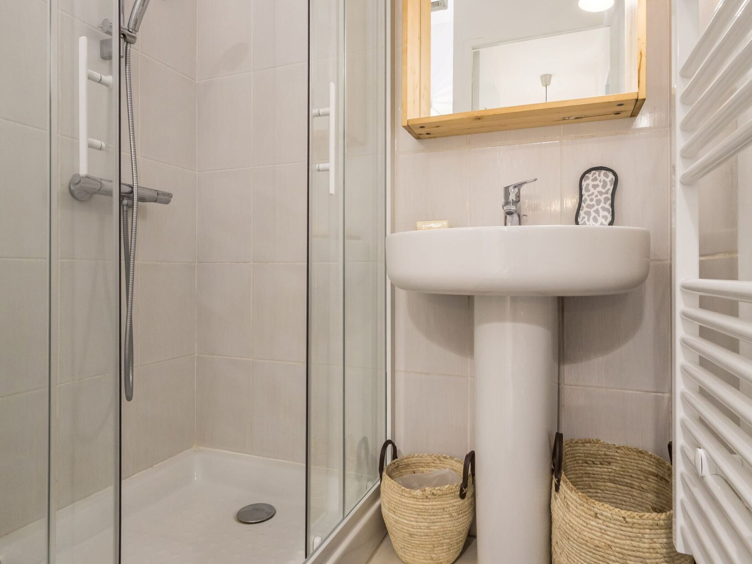 A modern bathroom with a glass shower enclosure, a pedestal sink, and two wicker baskets.