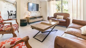 Un salon avec un canapé en cuir marron, une table basse en bois et un téléviseur fixé à un mur à texture.
