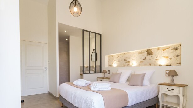 Une chambre moderne avec un grand lit, une table de chevet, une commode, un miroir et un luminaire fixé au mur.