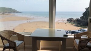 A room with a view of a beach, a table, and wicker chairs. - Stunning Beach Front Apartment in Caswell Swansea (Swansea)