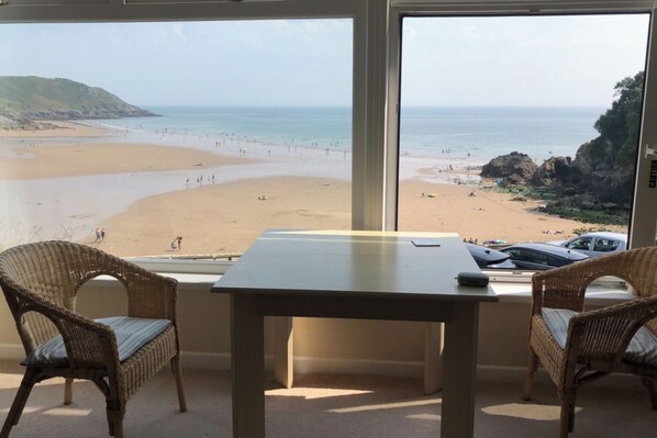 Ein Zimmer mit Blick auf einen Strand, einem Tisch und Korbstühle.