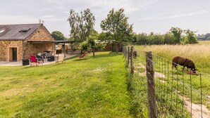 Un bâtiment en pierre doté d’un patio couvert, d’un espace clos où se trouve un mouton, et d’un champ herbeux.