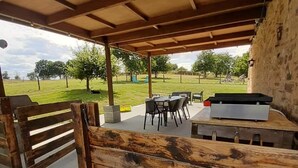 Un espace extérieur aménagé avec une terrasse, un banc en bois, une table avec des chaises et un barbecue.