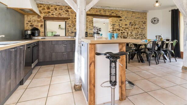 Une cuisine aux murs en pierre, avec des poutres en bois, un tabouret de bar et un coin repas équipé de chaises.