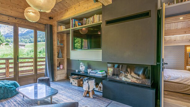 Um interior moderno com lareira, estantes de madeira com livros, uma mesa de centro de vidro e vista para o exterior.