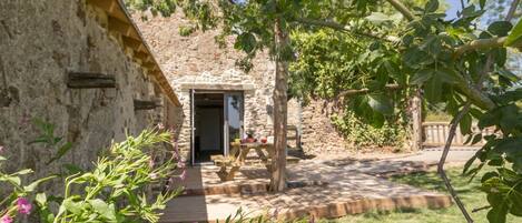 A stone building with a wooden door, a picnic table, and a garden with flowers.