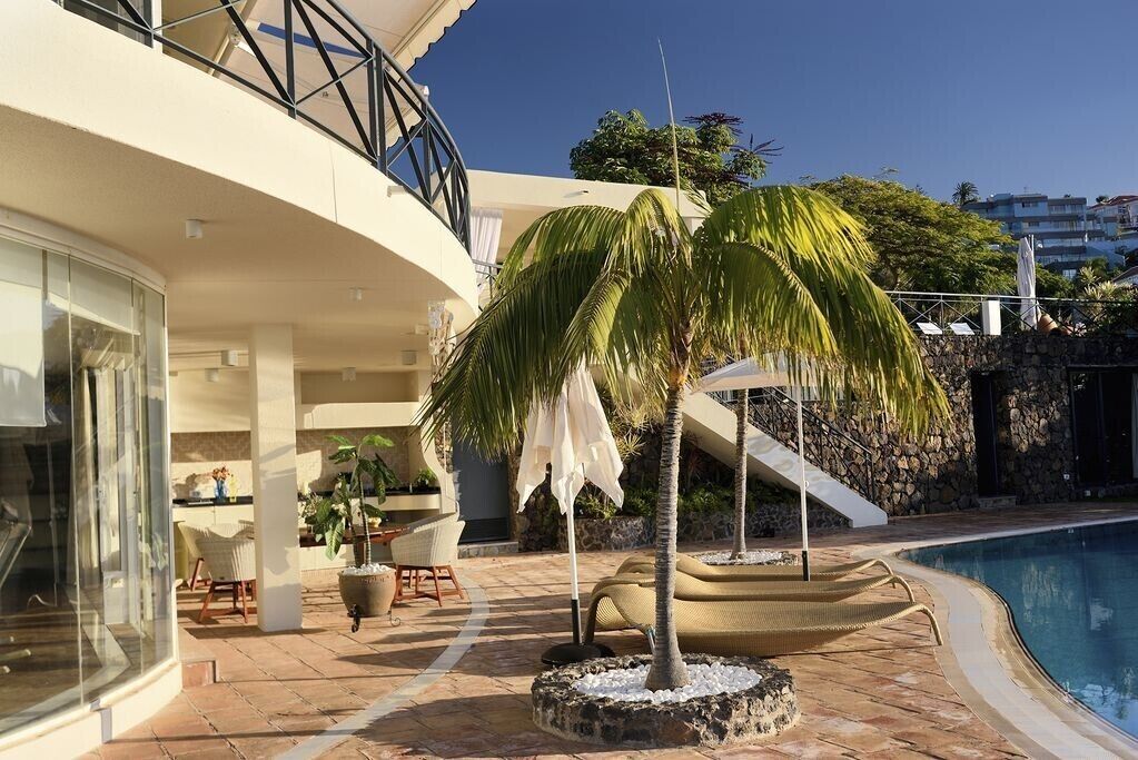 Un edificio moderno con piscina, mobiliario exterior y una palmera.