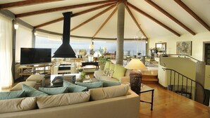 A spacious living area with a high ceiling, wooden beams, a large black fireplace, a sofa with cushions, a television, and a dining area with a table and chairs. - Luxury Villa Bahía with Infinity Pool, Panorama View, Sauna & Fitness Area (El Sauzal)