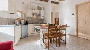 A modern kitchen with white cabinetry, wooden beams, a dining table with chairs, and a red chair. - Holiday Apartment "Casa di Ada" with Mountain Views and Wi-Fi (Segonzano)