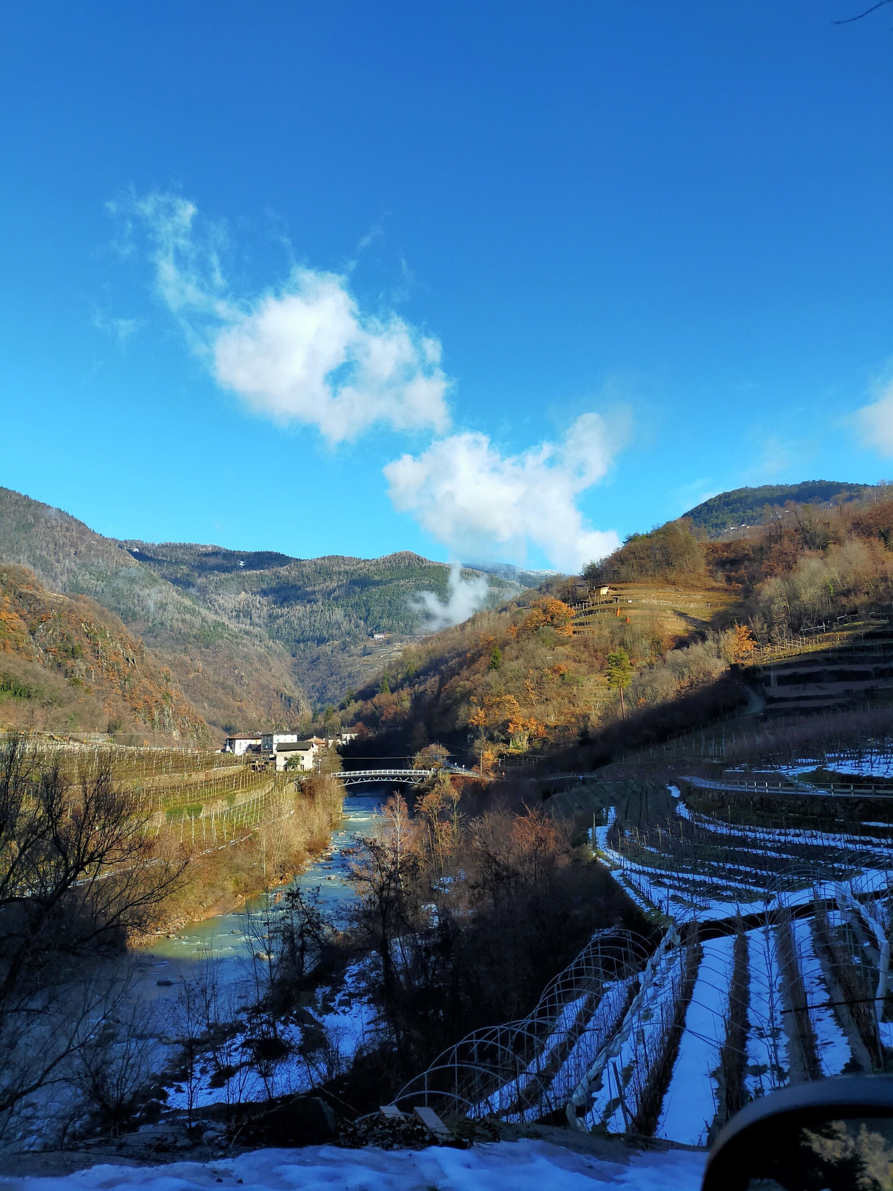 A river valley with a bridge, snow-covered fields, and a mountain backdrop.