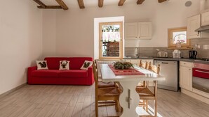 A compact living space with a red sofa, a dining table with chairs, a kitchen area with white cabinets, and a window with a view of the outside. - Holiday Apartment "Casa di Ada" with Mountain Views and Wi-Fi (Segonzano)