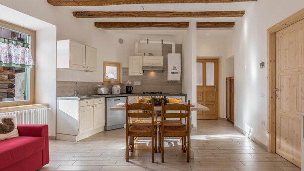 A modern kitchen with wooden beams, white cabinets, and a dining area with two wooden chairs. - Holiday Apartment "Casa di Ada" with Mountain Views and Wi-Fi (Segonzano)