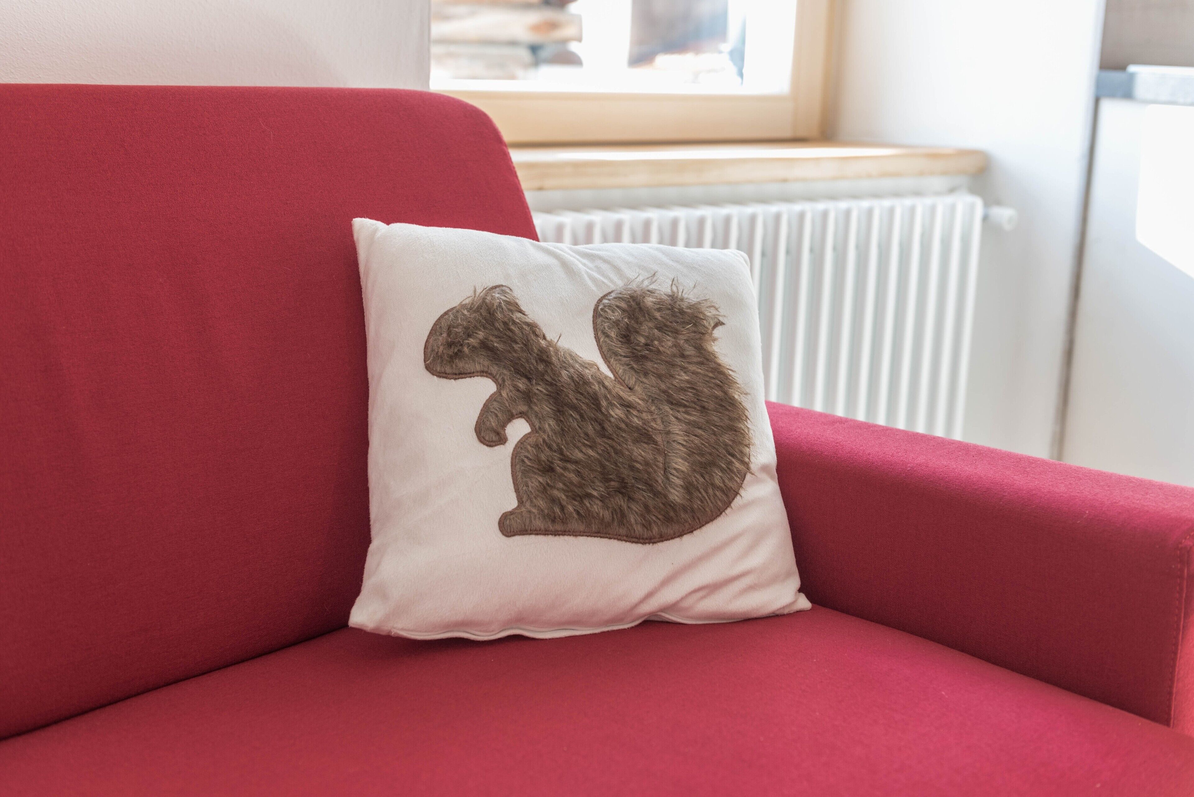 Un divano rosso con un cuscino bianco con un disegno raffigurante uno scoiattolo.