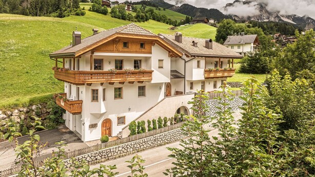 A two-story chalet with a balcony, stone steps, and a view of the surrounding hills. - Holiday Apartment "Désirée Dolasilla" with Balcony, Mountain View, Wi-Fi & TV (St. Vigil)