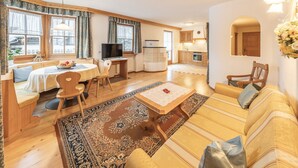 A cozy living room with a sofa, a coffee table, a dining table with chairs, a TV, and a kitchen area. - Holiday Apartment "Désirée Dolasilla" with Balcony, Mountain View, Wi-Fi & TV (St. Vigil)