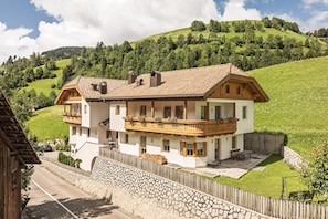 A two-story house with a balcony, a stone wall, and a grassy yard.