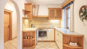 Een keuken met houten kastjes, een betegelde achterwand, een inbouwoven en een raam met gordijnen.