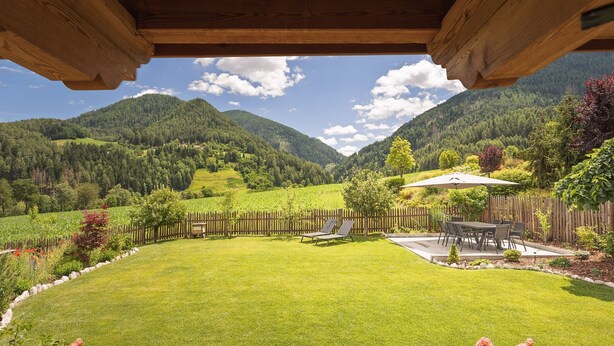 Une terrasse en bois offrant une vue sur une vallée verdoyante et luxuriante ainsi que sur des montagnes.