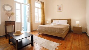 A bedroom with a wooden bed, a nightstand, a bedside table, a chair, a window with curtains, and a vase with dried flowers. - Home with Terrace in Heart of old Town of Chania (Chania)