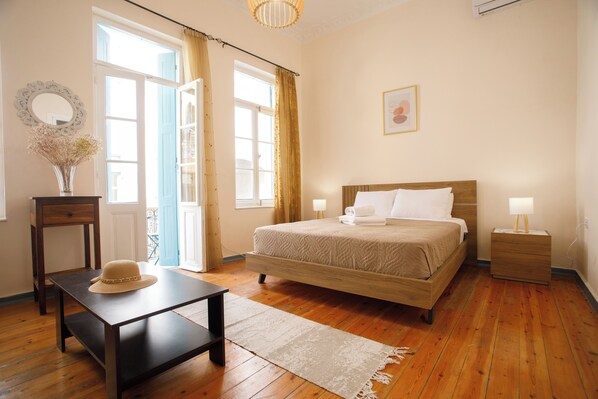 A bedroom with a wooden bed, a nightstand, a bedside table, a chair, a window with curtains, and a vase with dried flowers.