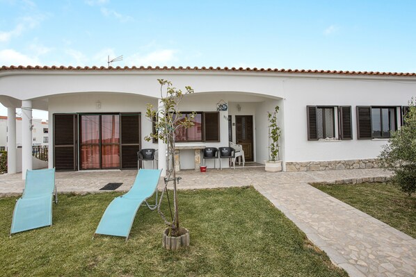 A house with a patio, two blue lounge chairs, a small tree, and a stone pathway.